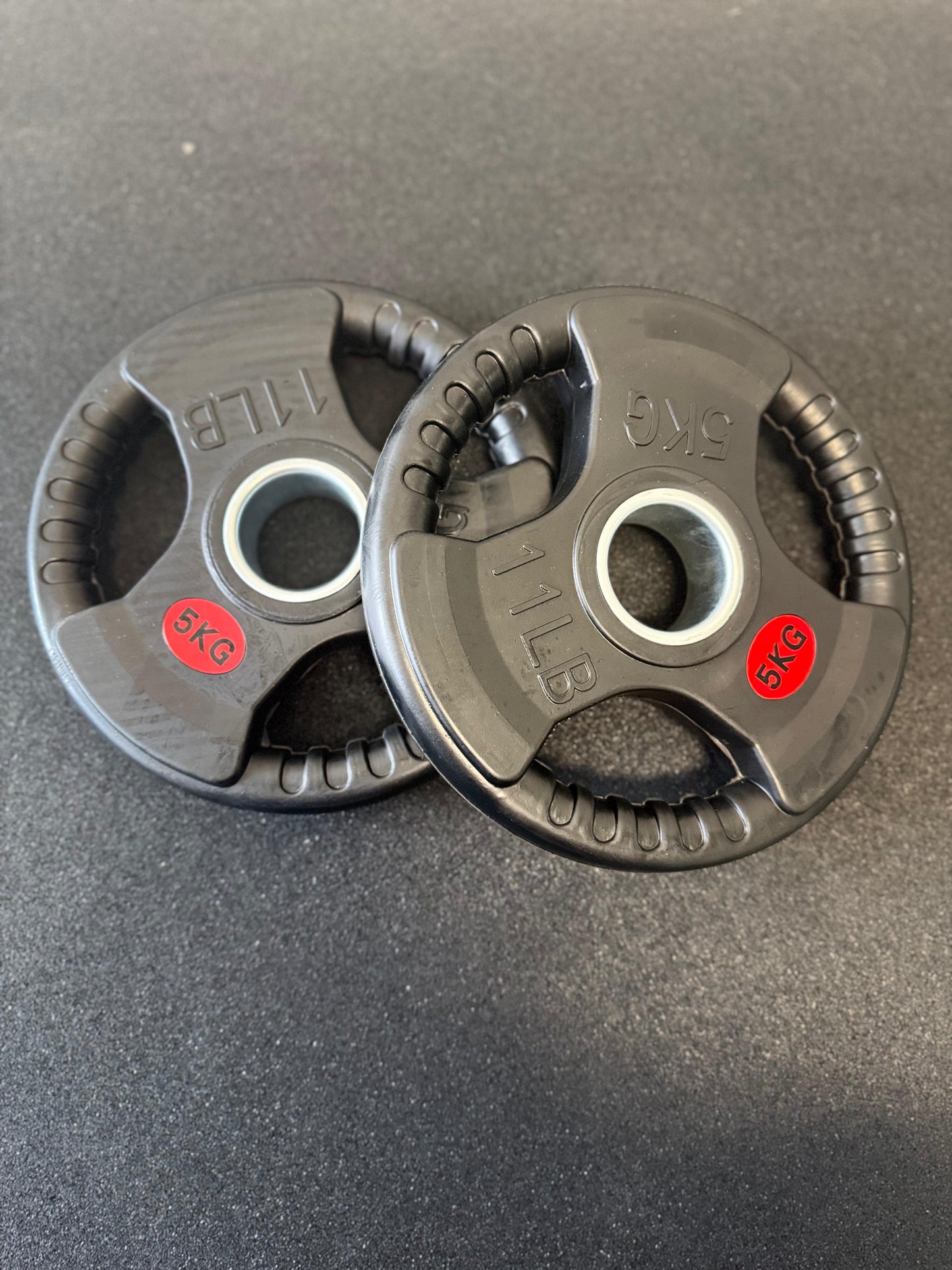 Two black weight plates with red labels on a dark surface