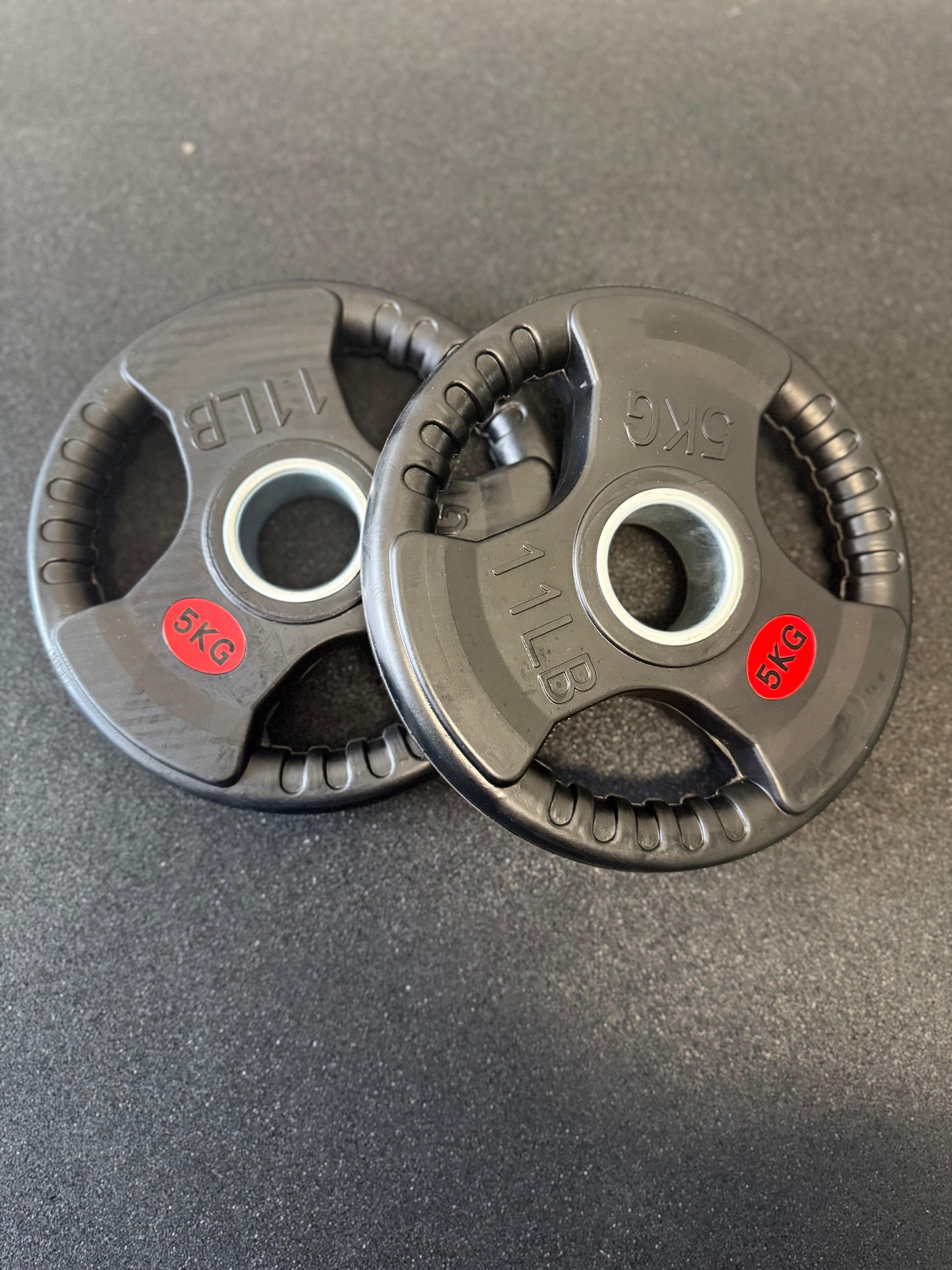 Two black weight plates with red labels on a dark surface