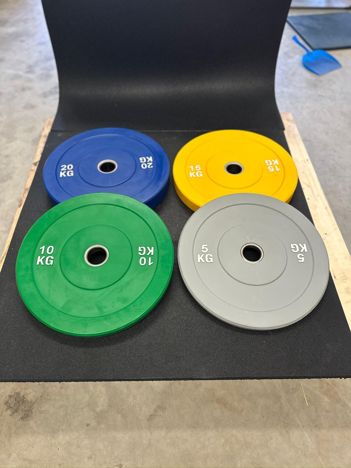 Four weight plates in blue, yellow, green, and gray on a black mat.